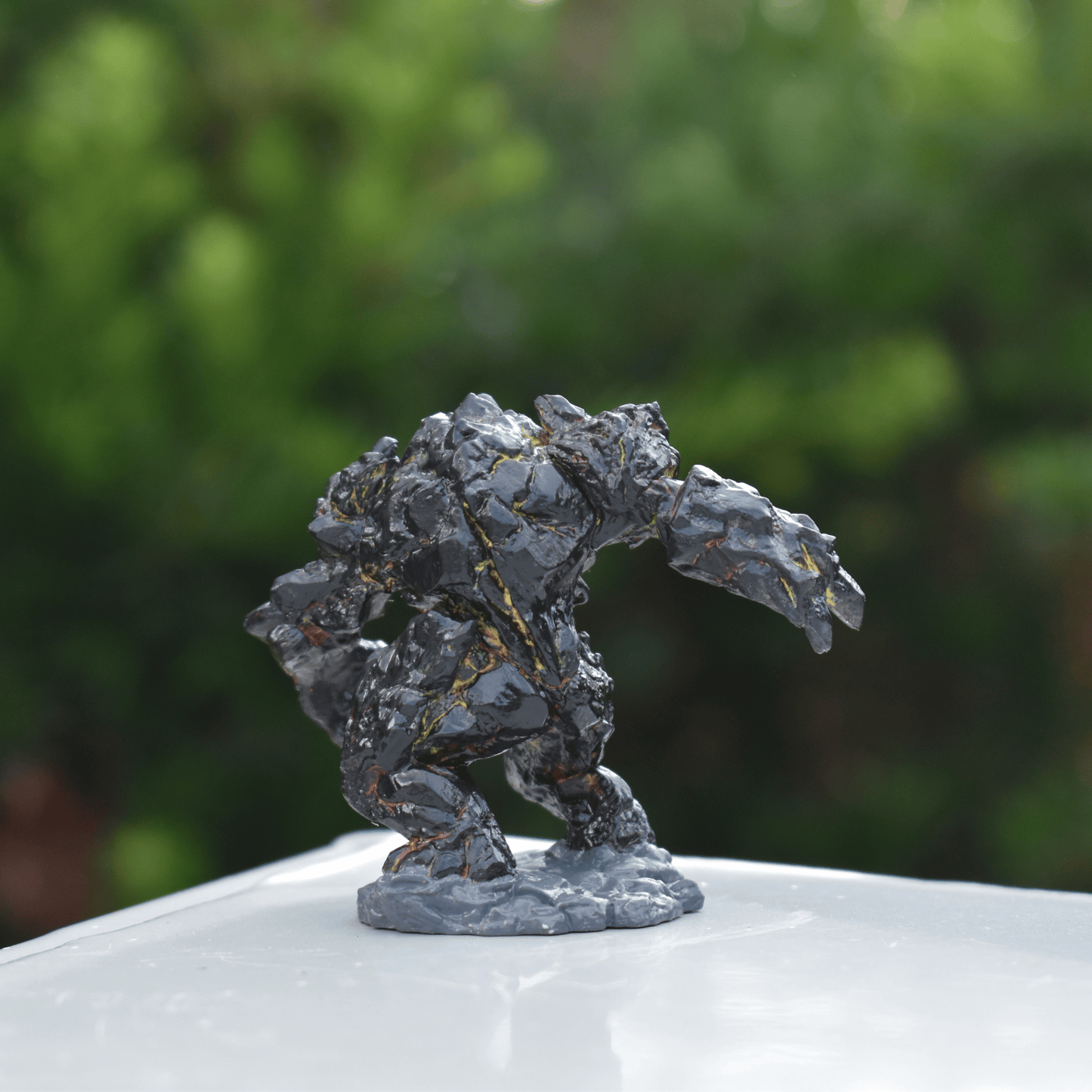 Side view of a hand-painted Black Magma Golem miniature, showcasing cracked molten veins and rugged volcanic rock texture.