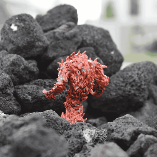 Rear view of a hand-painted fire elemental miniature, showcasing the textured, flame-like sculpting and molten details. The figure stands amidst a bed of rough, black lava rocks.