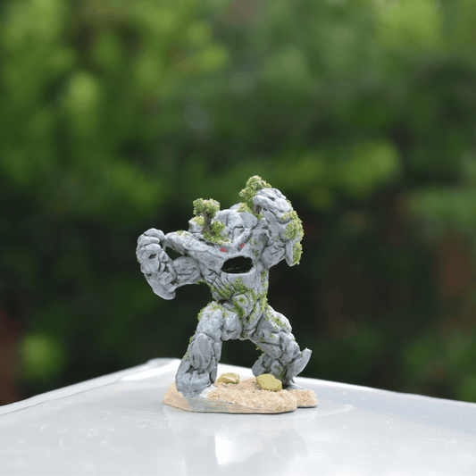 Hand-painted Earth Elemental miniature with glowing red eyes and mossy stone texture, posed with arms raised on a sandy base.