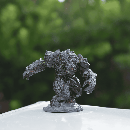 Hand-painted Black Magma Golem miniature standing in a battle stance on a white surface, with glossy obsidian textures and glowing magma cracks.