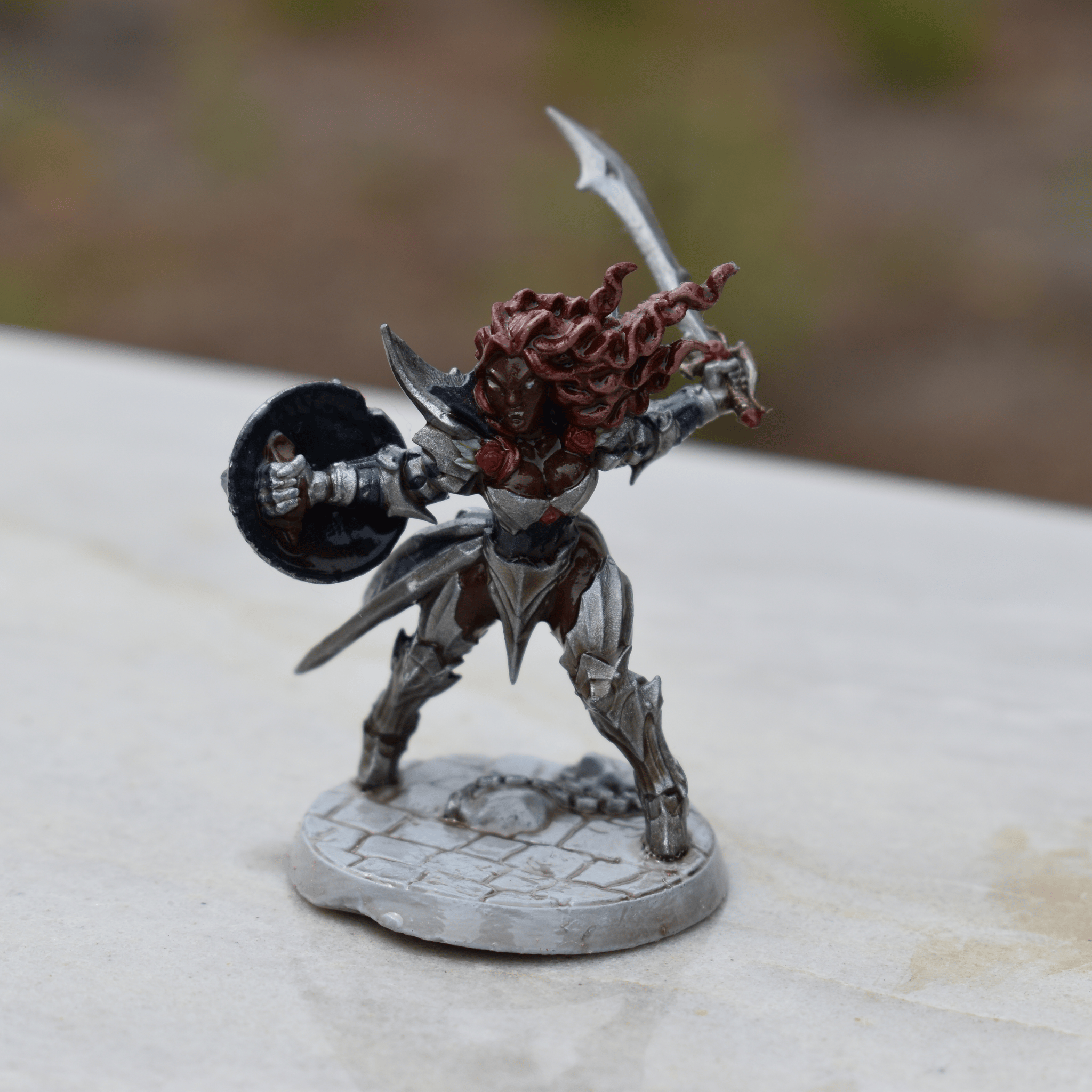Painted miniature of a female warrior in silver armor with red hair, armed with a sword and shield, on a stone-tile base.