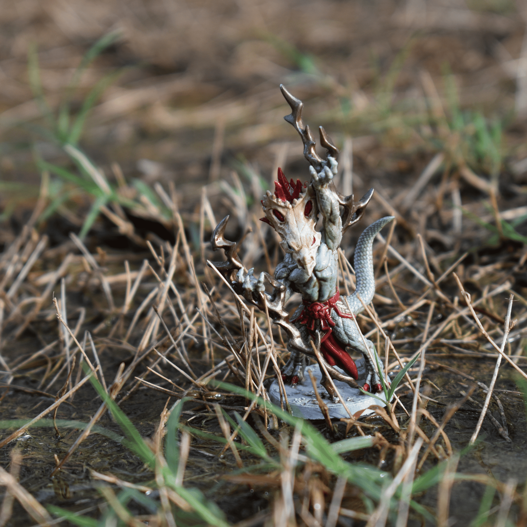 Hand-painted miniature of a reptilian spellcaster with a bone crown and red accents, posed in swampy grass terrain.