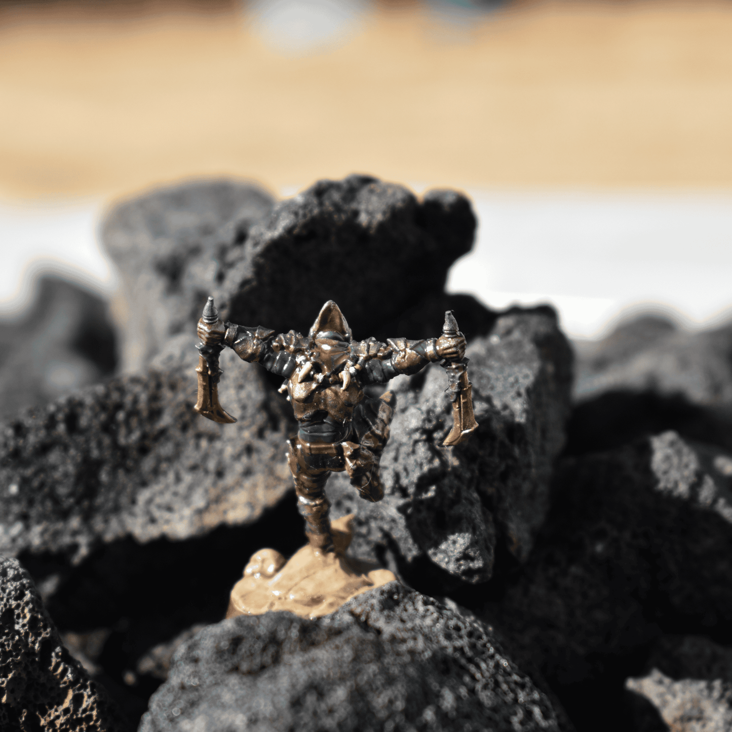 Dual-Blade Assassin miniature posed atop black volcanic rocks, mid-action with gold weapons and detailed green-and-bronze armor.