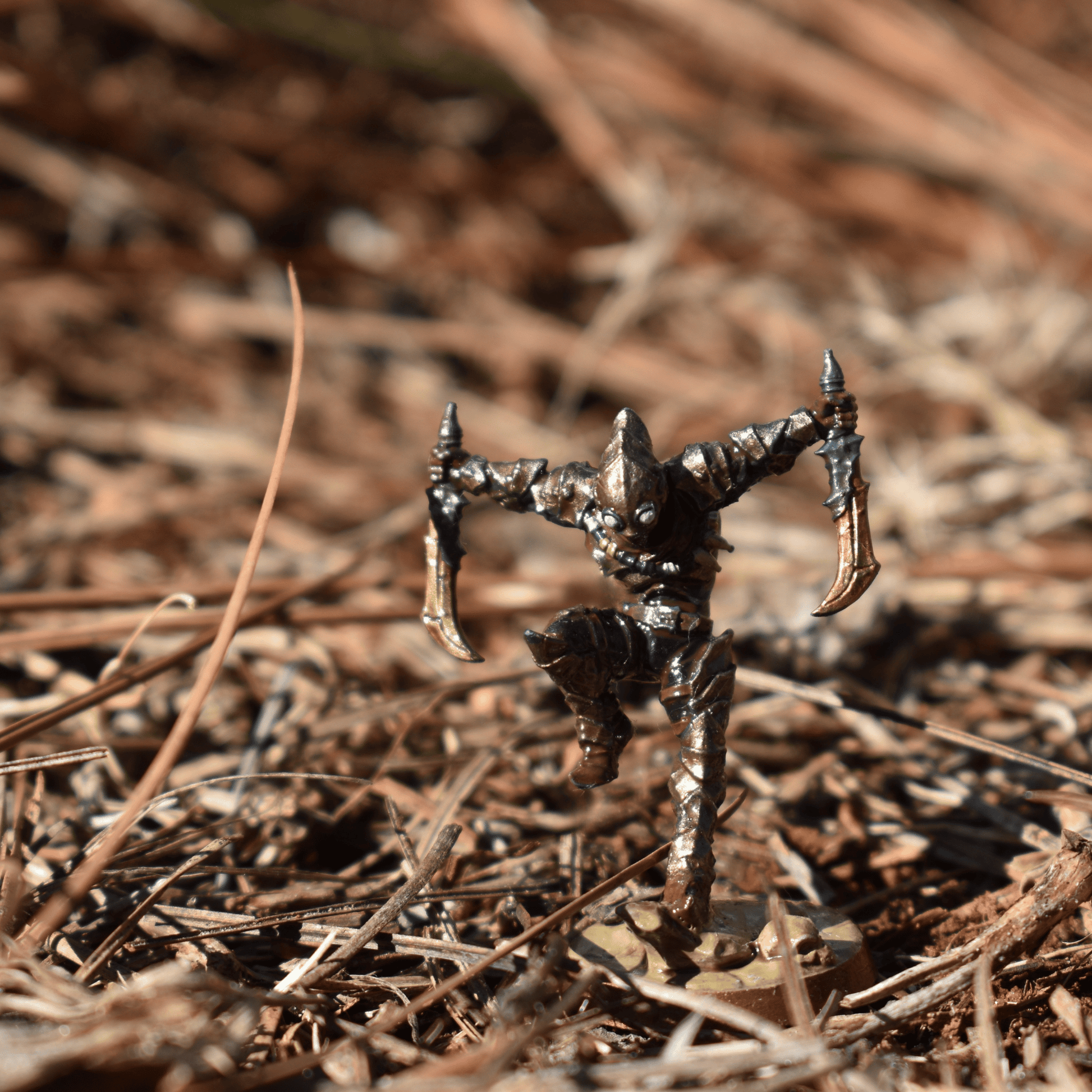 Hand-painted Dual-Blade Assassin miniature posed mid-leap with gold daggers, set against a forest floor with pine needles.