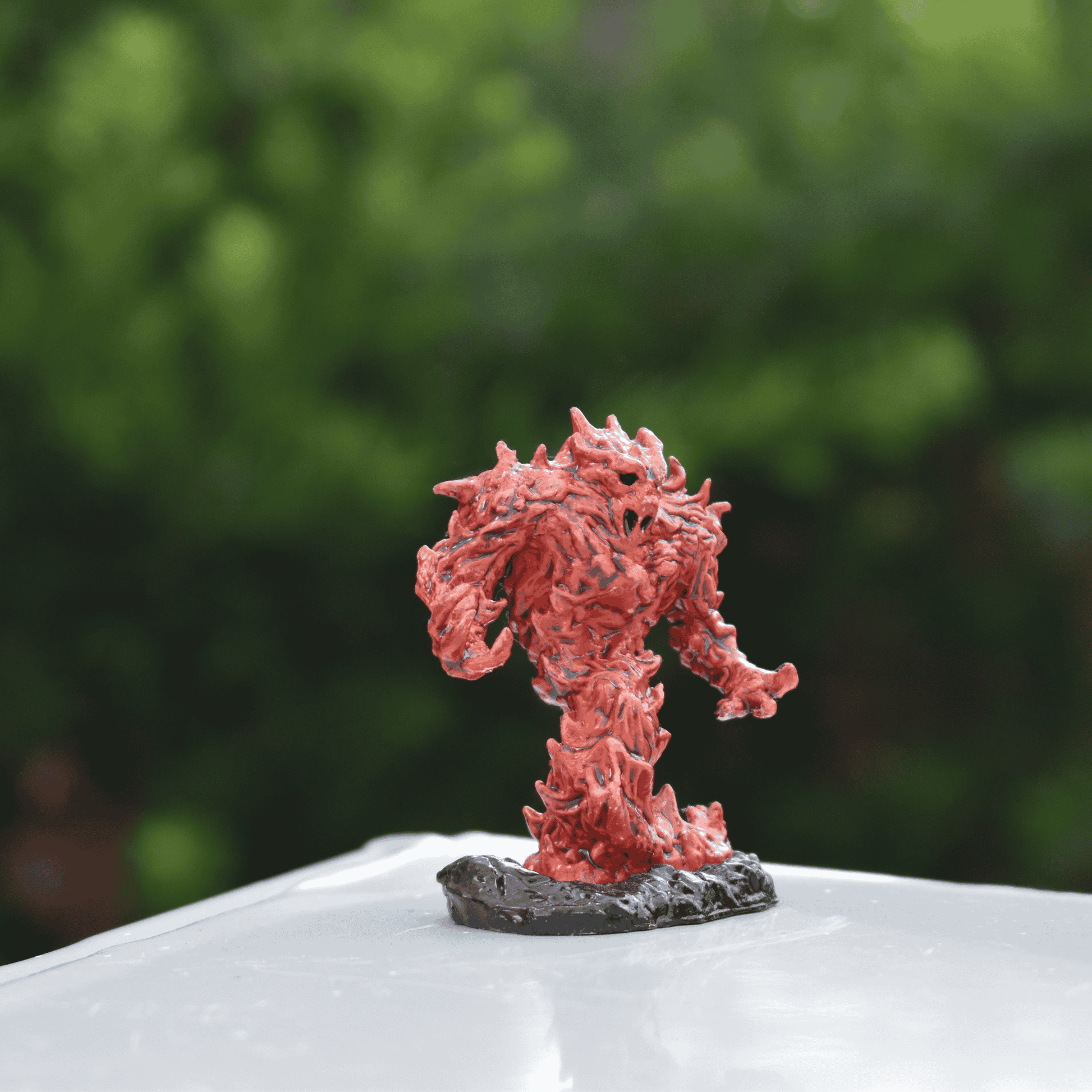 A hand-painted fire elemental miniature in ember-red and black tones, posed menacingly on a table. The figure appears to emerge from the rocky terrain with arms raised, ready for battle.