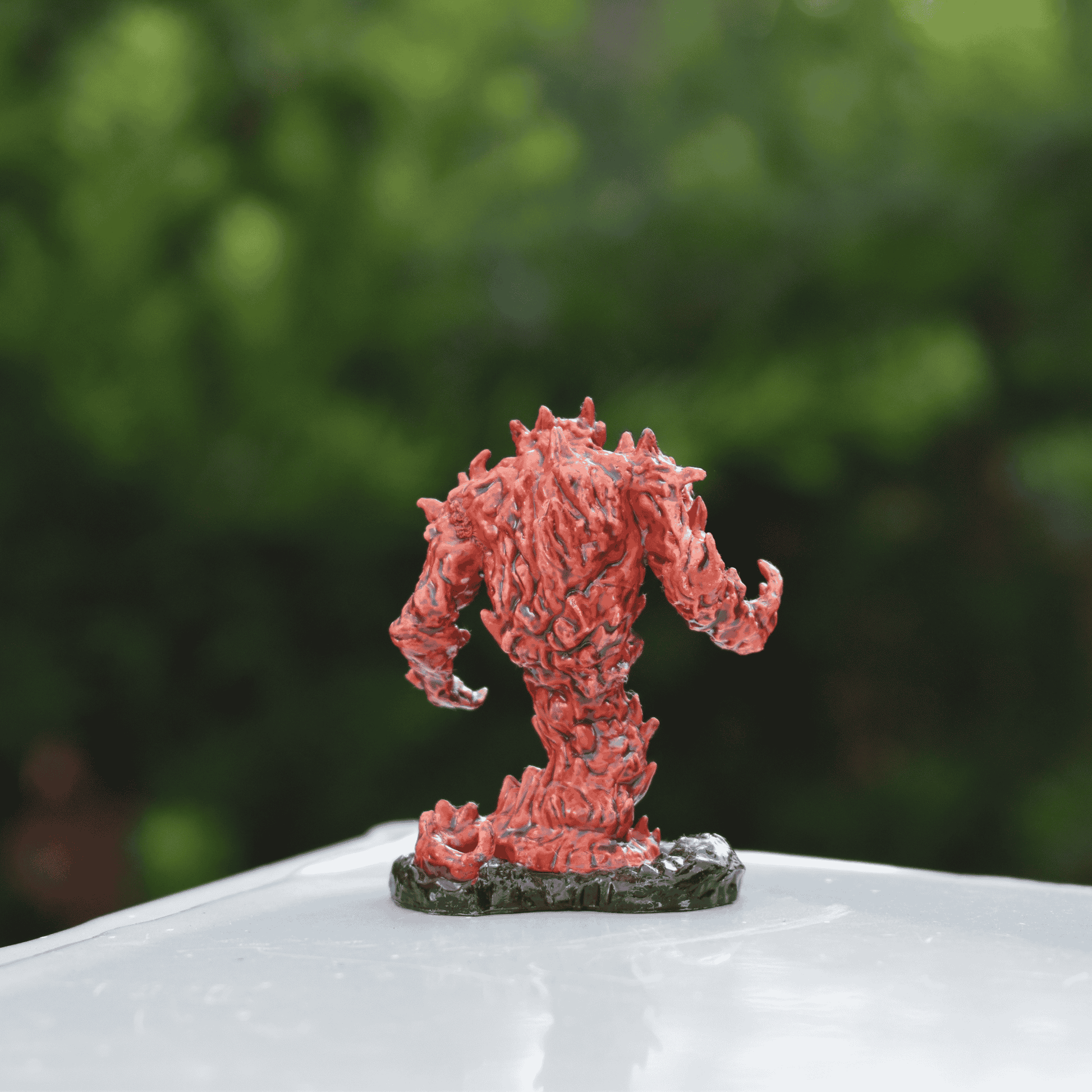A hand-painted fire elemental miniature in ember-red and black tones, posed menacingly on a table. The figure is facing the back.