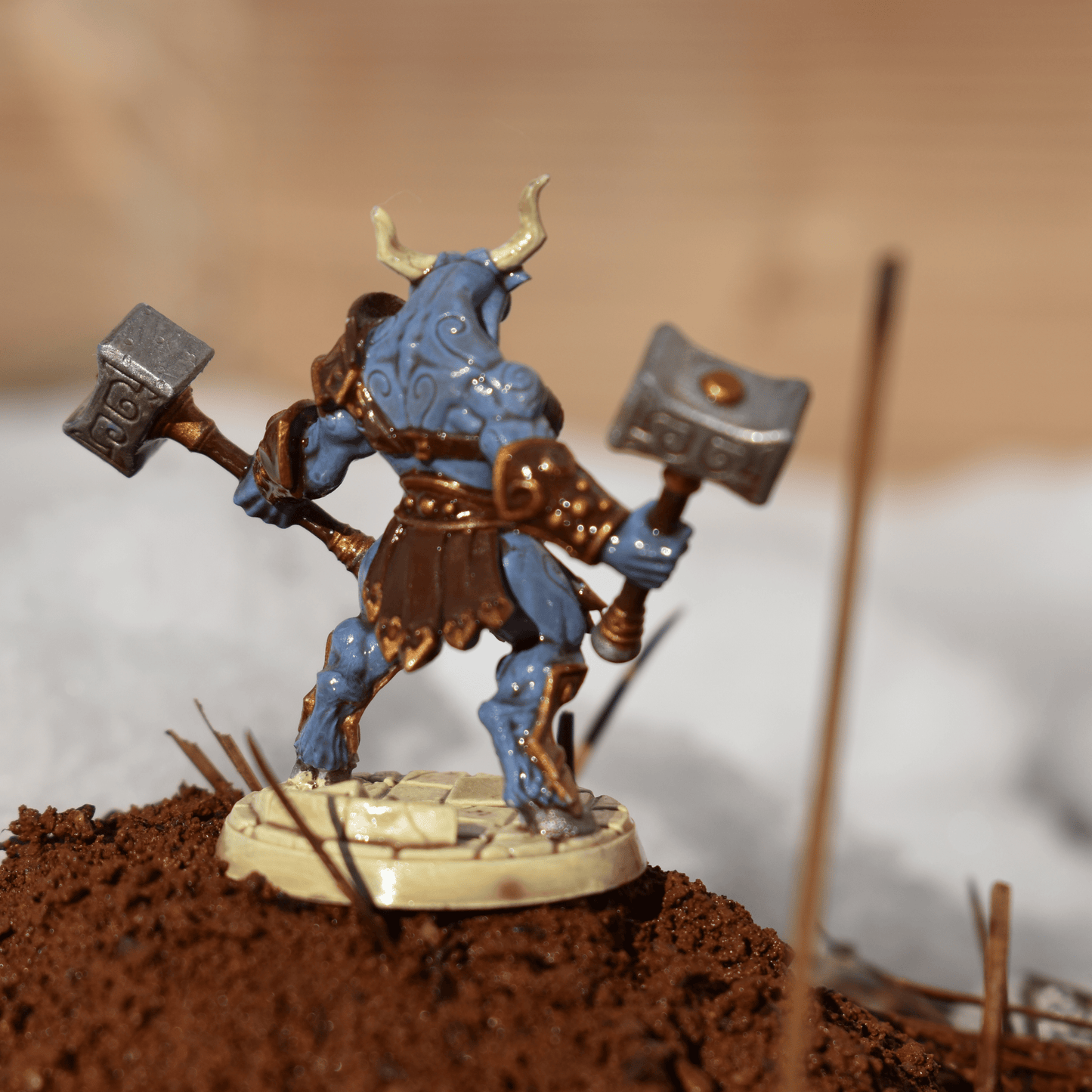 Back view of a hand-painted Minotaur miniature showing sculpted armor detail, swirling tattoos, and raised hammers against a snowy terrain.