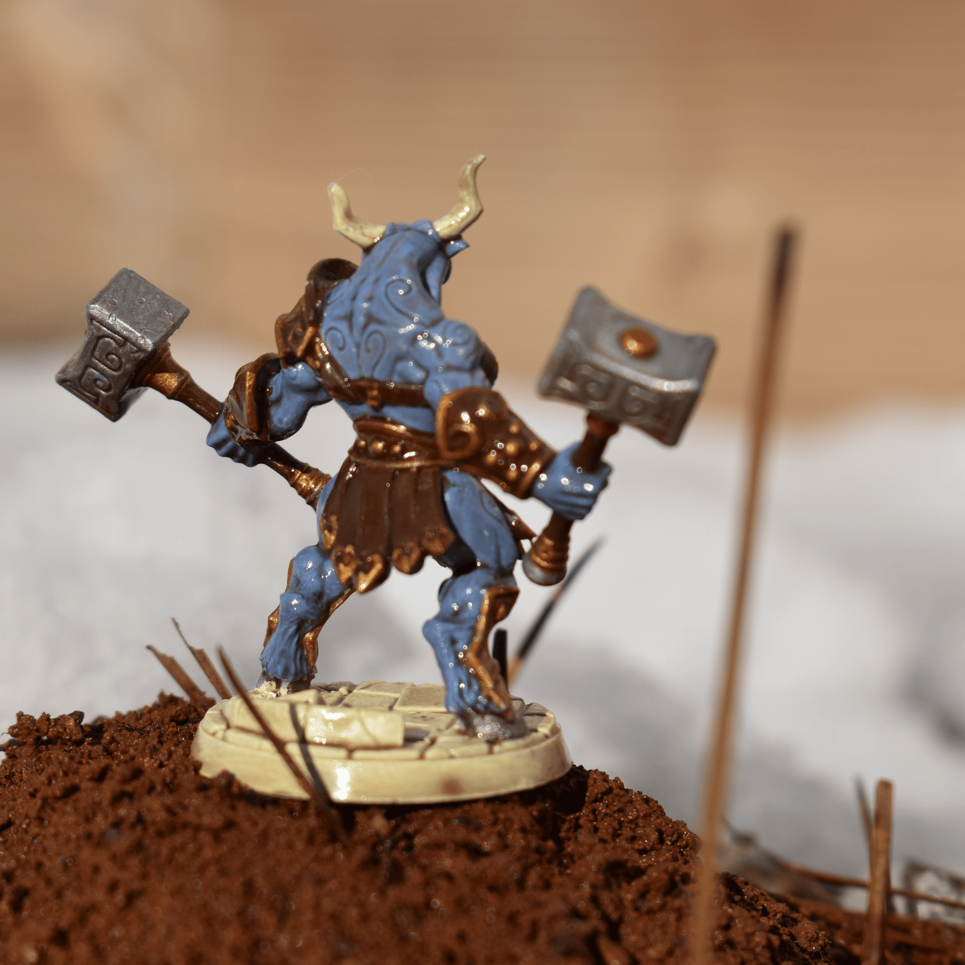 Back view of a hand-painted Minotaur miniature showing sculpted armor detail, swirling tattoos, and raised hammers against a snowy terrain.