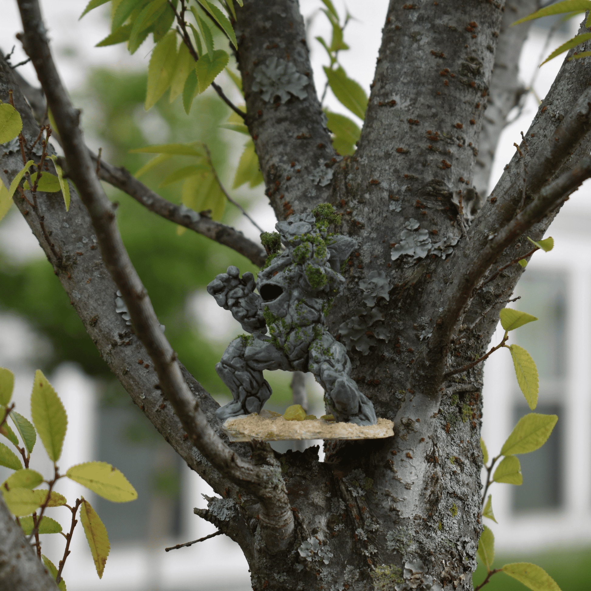 Earth Elemental miniature nestled in a tree branch, showcasing its hand-painted moss and rock textures in a natural outdoor setting.