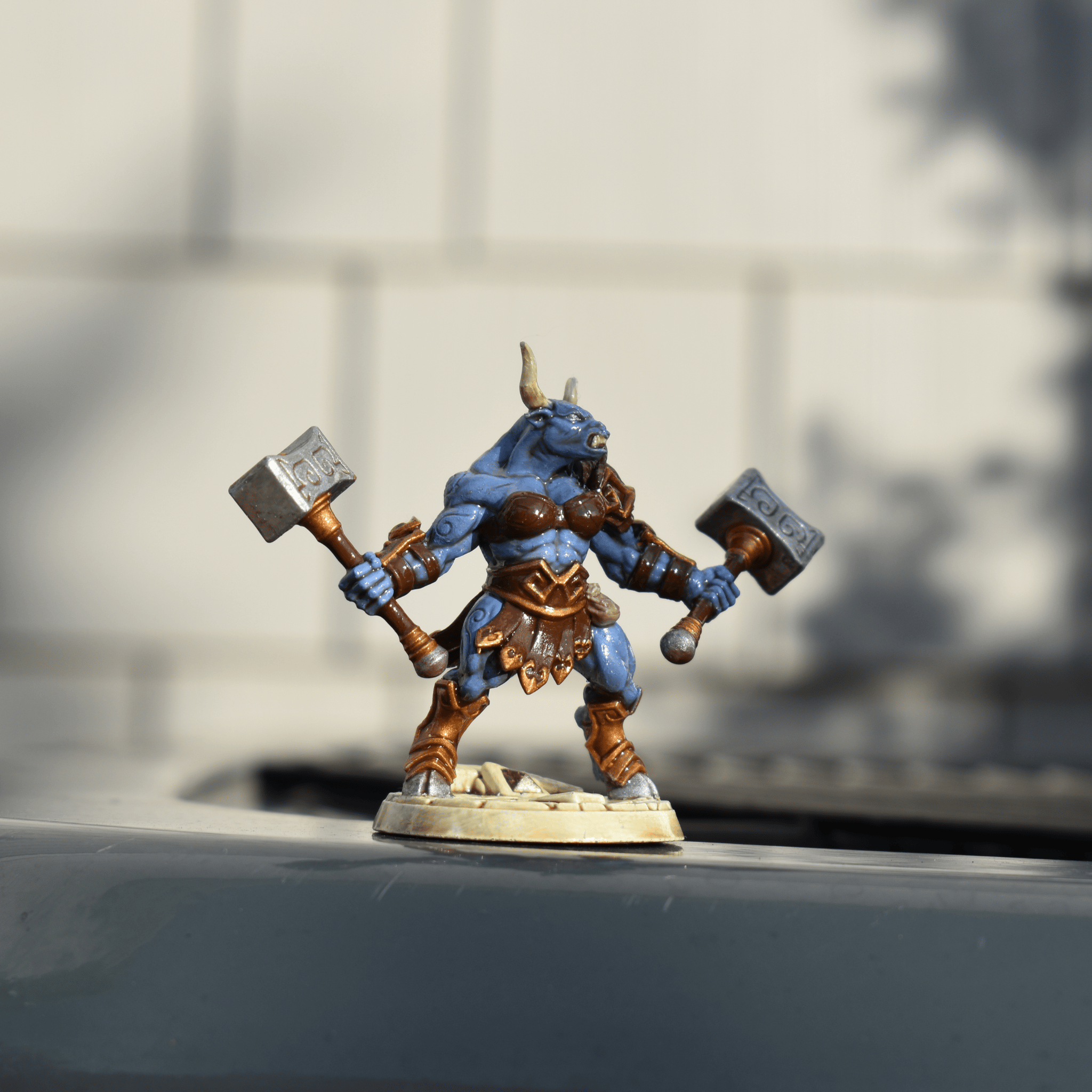Hand-painted miniature of a blue-skinned minotaur warrior wielding two hammers, standing on a sculpted base.